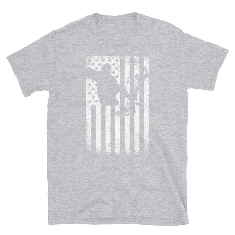May include: A light gray t-shirt featuring a distressed white graphic of an archer with a bow and arrow, set against a stylized American flag background. The design has a vintage, worn look.
