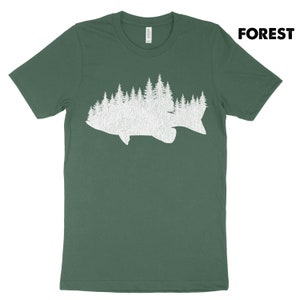 May include: Green t-shirt with a white graphic of a fish silhouette filled with a forest design. The word "FOREST" is printed in bold, black letters in the upper right corner. The shirt is made of a soft material.