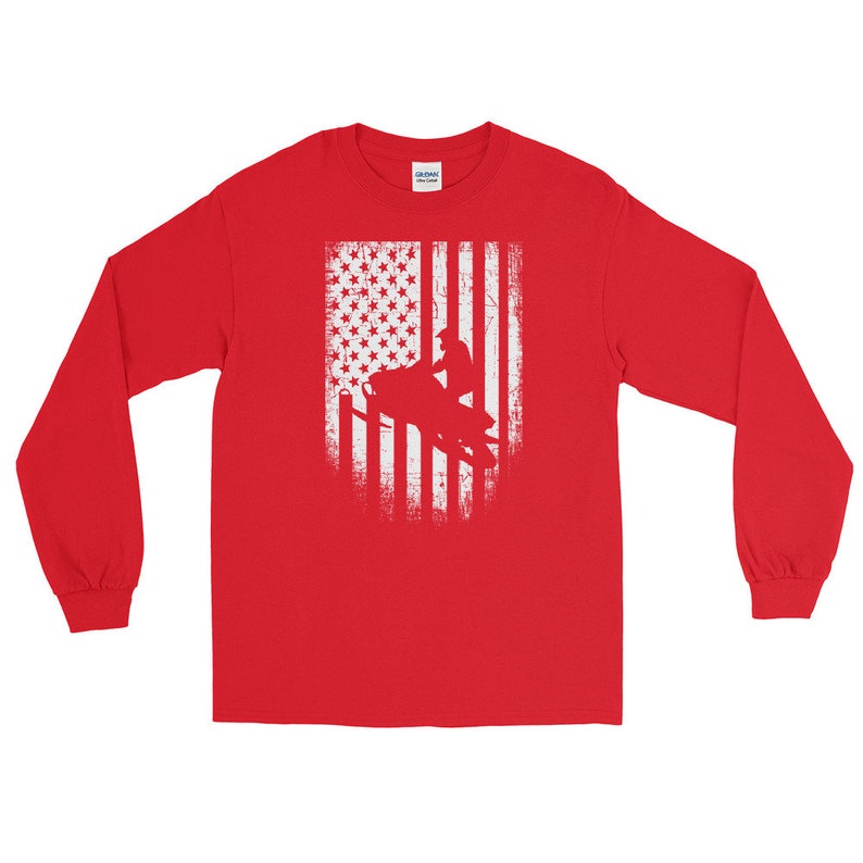 K&ouml;nnte beinhalten: Rotes Langarm-T-Shirt mit einem wei&szlig;en, abgenutzten amerikanischen Flaggen-Design, das die Silhouette einer Person auf einem Schneemobil zeigt.