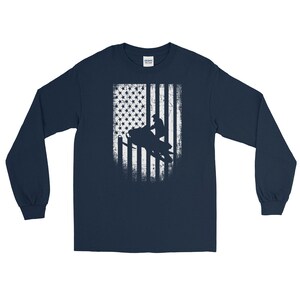 K&ouml;nnte beinhalten: Langarm-T-Shirt in Marineblau mit einem wei&szlig;en, abgenutzten amerikanischen Flaggen-Design, das die Silhouette einer Person auf einem Schneemobil zeigt.