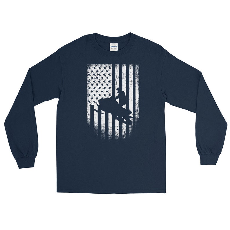 K&ouml;nnte beinhalten: Langarm-T-Shirt in Marineblau mit einem wei&szlig;en, abgenutzten amerikanischen Flaggen-Design, das die Silhouette einer Person auf einem Schneemobil zeigt.
