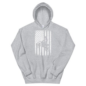 May include: A gray hooded sweatshirt with a white distressed American flag design featuring a silhouette of a person working on a power line.