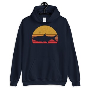 May include: A navy blue hoodie with a vintage-style sunset graphic featuring a silhouette of a tarpon fish. The sunset is in shades of yellow, orange, and red.