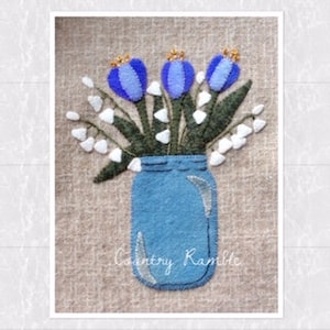 May include: A blue glass jar filled with a bouquet of blue and white flowers. The flowers are arranged in a rustic style and the jar has a simple, country charm. The text "Country Ramble" is visible at the bottom of the image.