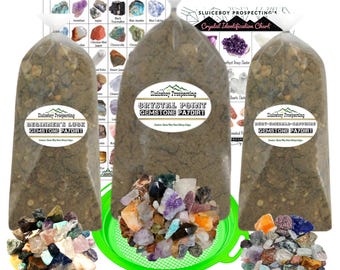 Op de afbeelding: Drie zakken aarde met verschillende edelstenen. De zakken zijn gelabeld met "Beginner's Luck Gemstone Paydirt", "Crystal Point Gemstone Paydirt" en "Rust-Emerald-Sapphire Gemstone Paydirt". Een groene plastic bak met een gaasbodem is gevuld met verschillende edelstenen.