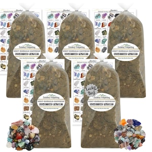 May include: Five clear plastic bags filled with brown dirt and labeled "Rusty Emerald & Sapphire Gemstone Paydirt". Each bag is accompanied by a gemstone identification chart. The bags are arranged in a row, with a "Lucky Bag" label in the center.