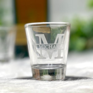 Op de afbeelding: Een helder glazen shotglas met de letter "M" en de naam "MICHAEL" gegraveerd in de zijkant.