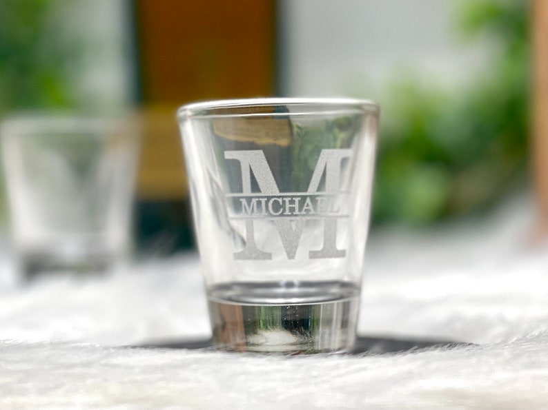 Op de afbeelding: Een helder glazen shotglas met de letter "M" en de naam "MICHAEL" gegraveerd in de zijkant.