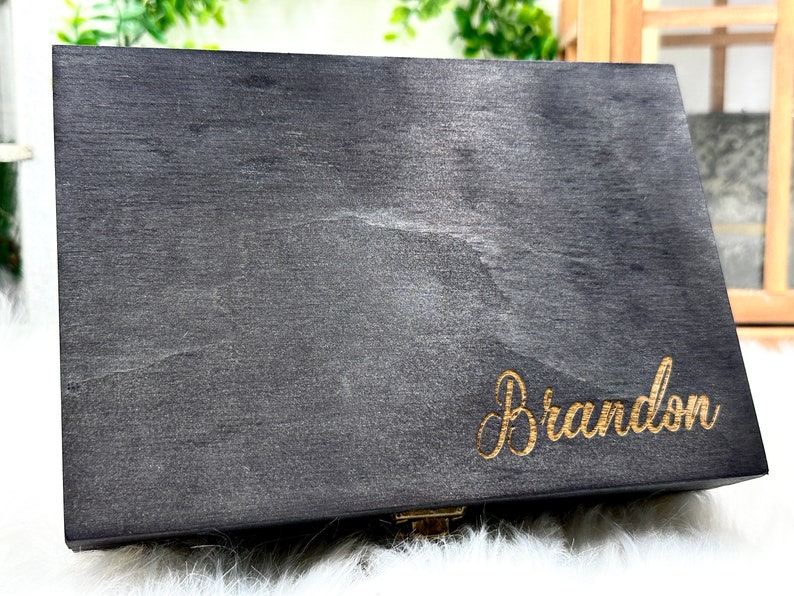 May include: A dark gray wooden box with a gold latch and the name "Brandon" engraved in gold lettering.