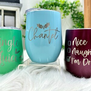 May include: Three stainless steel wine tumblers with Christmas-themed designs. The green tumbler says "Jingle Juice", the blue tumbler says "Chantel" with a holly sprig, and the purple tumbler says "Nice Naughty I'm Drunk" with a checkmark next to "I'm Drunk".