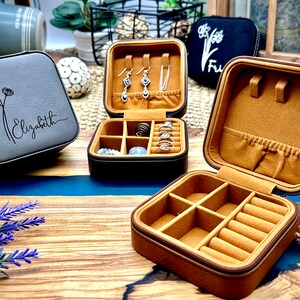 Puede incluir: Tres cajas de joyer&iacute;a de imitaci&oacute;n de cuero gris y marr&oacute;n con compartimentos para anillos, pendientes y collares. Una caja est&aacute; abierta y muestra los compartimentos interiores. Una caja tiene el nombre "Elizabeth" grabado en la tapa.