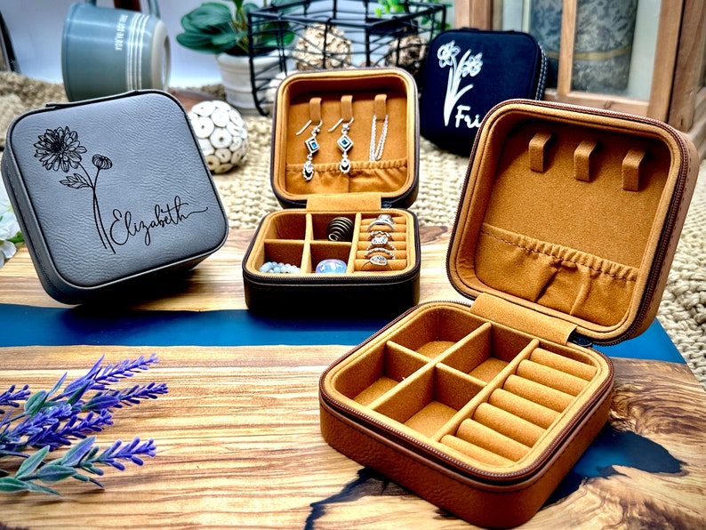 Puede incluir: Tres cajas de joyer&iacute;a de imitaci&oacute;n de cuero gris y marr&oacute;n con compartimentos para anillos, pendientes y collares. Una caja est&aacute; abierta y muestra los compartimentos interiores. Una caja tiene el nombre "Elizabeth" grabado en la tapa.