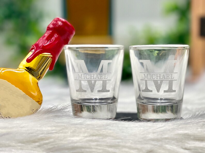 Op de afbeelding: Twee glazen shotglazen met een zilveren rand. Elk glas is gegraveerd met de letter "M" en de naam "Michael" eronder.