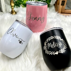May include: Three personalized stainless steel wine tumblers with lids. The tumblers are pink, white, and black. The names "Jenny", "Olivia", and "Melissa" are engraved on the tumblers.