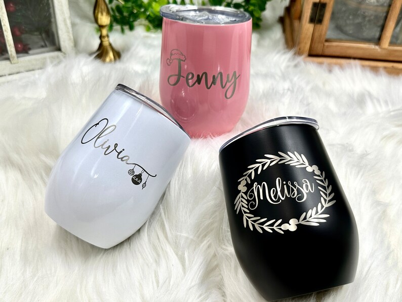 May include: Three personalized stainless steel wine tumblers with lids. The tumblers are pink, white, and black. The names "Jenny", "Olivia", and "Melissa" are engraved on the tumblers.
