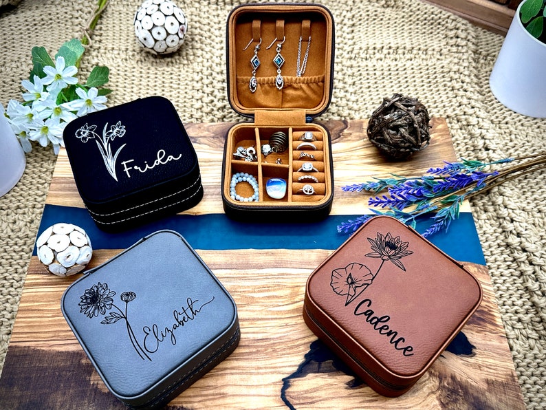 Puede incluir: Tres cajas de joyer&iacute;a personalizadas con diferentes dise&ntilde;os florales y nombres: Frida, Elizabeth y Cadence. Las cajas est&aacute;n hechas de piel sint&eacute;tica y tienen una combinaci&oacute;n de colores marr&oacute;n, gris y negro.