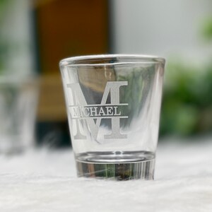 Op de afbeelding: Een helder glazen shotglas met een gegraveerde initial "M" en de naam "MICHAEL" eronder.