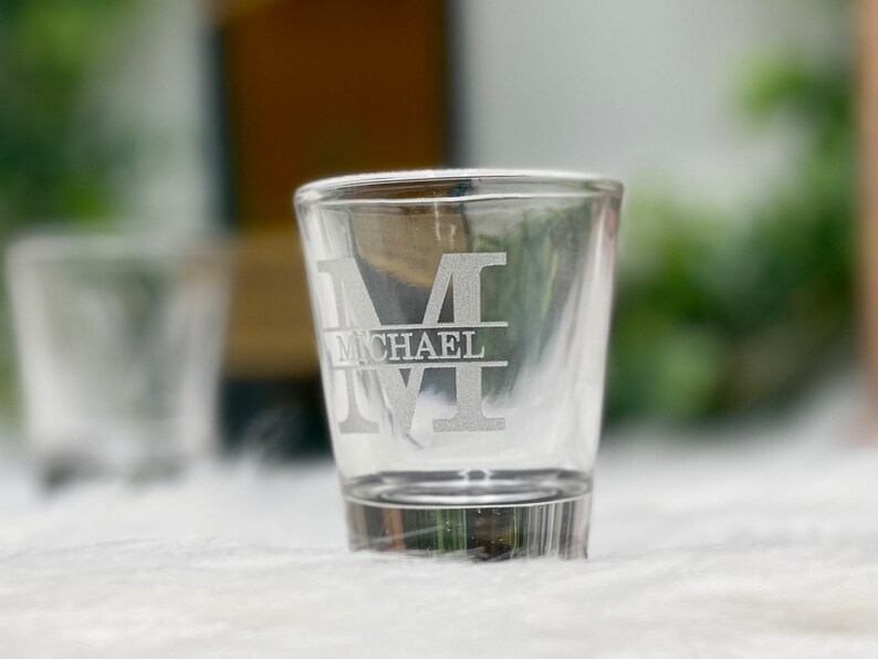 Op de afbeelding: Een helder glazen shotglas met een gegraveerde initial "M" en de naam "MICHAEL" eronder.