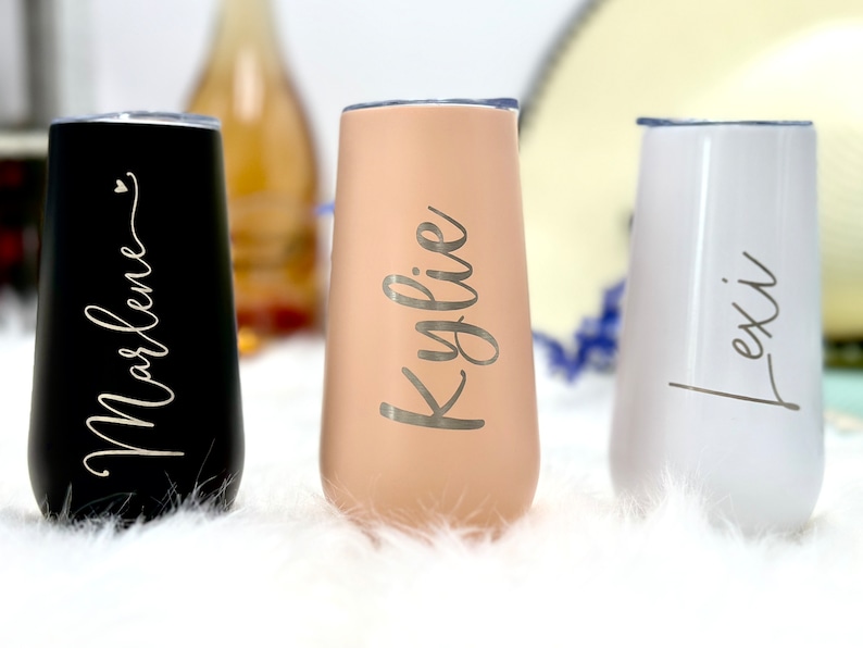 May include: Three stemless tumblers with clear lids, featuring a matte black finish with the name Marlene, a matte beige finish with the name Kylie, and a glossy white finish with the name Lexi, all written in a cursive script font.