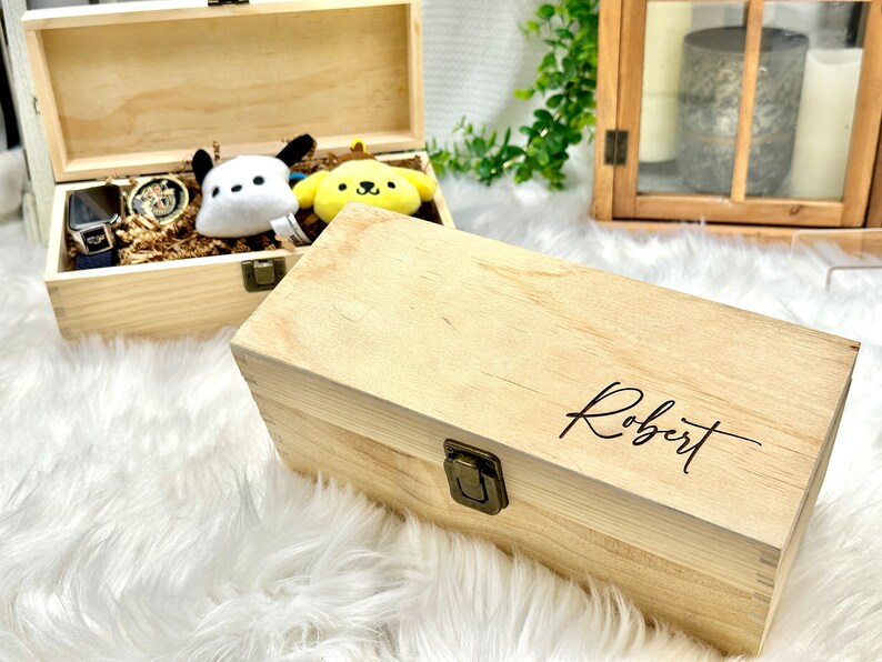 May include: Two wooden boxes with lids. The top box is open and contains a watch, a stuffed animal, and a small toy. The bottom box is closed and has the name "Robert" engraved on the top.