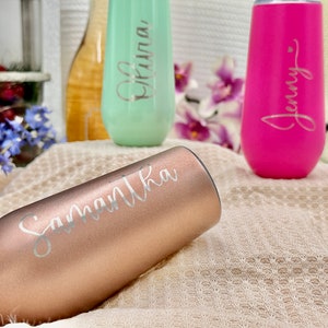 May include: Three stainless steel stemless champagne flutes with a matte finish. One is rose gold with the name Samantha, one is mint green with the name Olivia, and one is hot pink with the name Jenny. Each flute features custom script lettering.