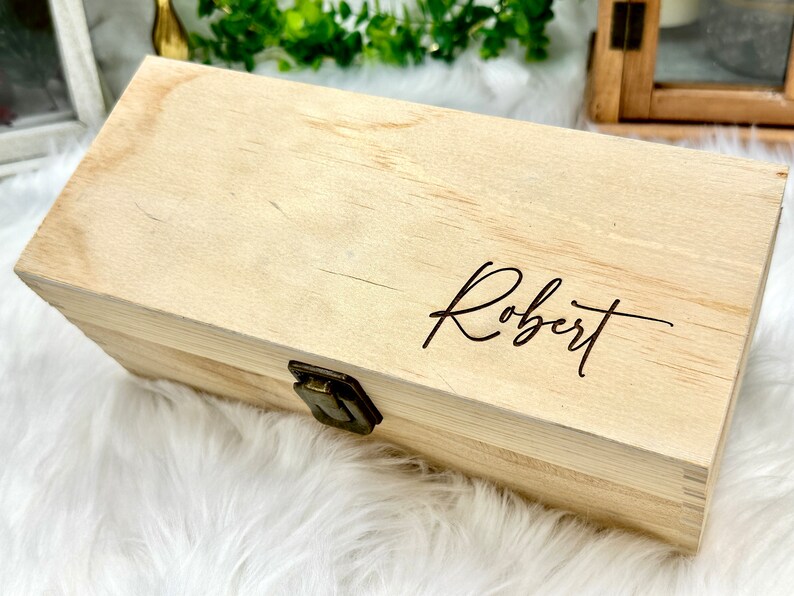 May include: A wooden box with a hinged lid and a brass latch. The box is engraved with the name "Robert".