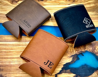 May include: Three personalized leather can coolers. The first is brown with the name "Adrian" and the text "Greensman". The second is brown with the initials "JE". The third is black with the initial "R" in a diamond shape and the name "Ryan" below.