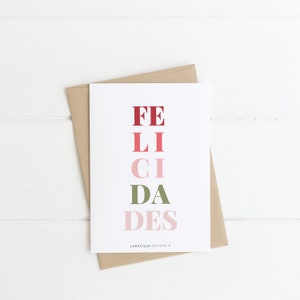Puede incluir: Una tarjeta blanca con un sobre marrón. La tarjeta tiene la palabra "FELICIDADES" escrita en letras verticales rojas, rosas y verdes.