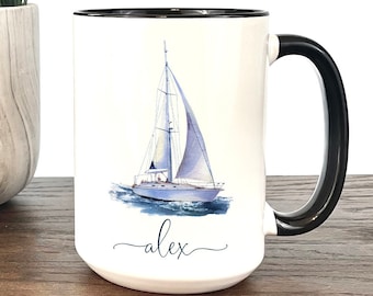 May include: White ceramic coffee mug with a black rim and handle. The mug features a watercolor illustration of a sailboat with the name "alex" written in cursive below it.