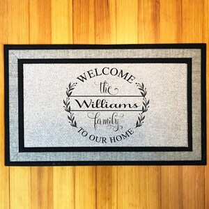 May include: A gray welcome mat with black trim and the text "Welcome the Williams family to our home" in a black circle with a wreath design.