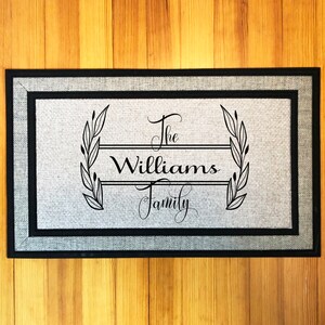 May include: A gray doormat with black trim and the text "The Williams Family" in a decorative font with a wreath design.