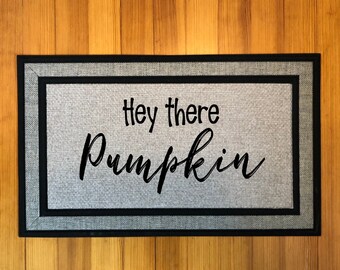 May include: A grey doormat with black trim and the text "Hey there Pumpkin" in black lettering.