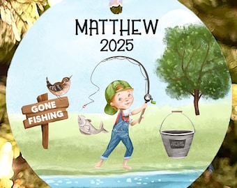 May include: Round Christmas ornament with a fishing theme. The ornament features a boy fishing, a sign that says "Gone Fishing", and the name "Matthew" with the year "2025". The ornament has a white ribbon for hanging.