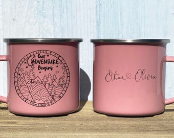 May include: Two pink enamel mugs with black text. One mug says "Our Adventure Begins" with a mountain and moon design. The other mug says "Ethan Olivia" with a heart symbol between the names.