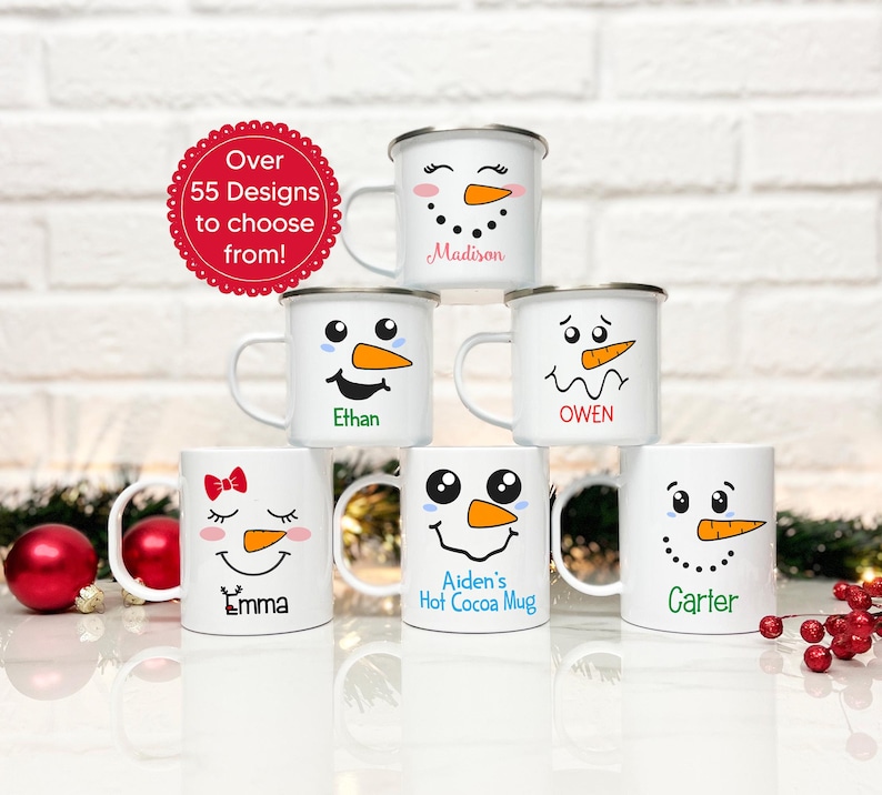 May include: Six white enamel mugs with snowman faces and personalised names. The mugs are stacked in a pyramid shape on a white surface. The names on the mugs are Madison, Ethan, Owen, Emma, Aiden's Hot Cocoa Mug, and Carter.