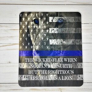 May include: A black and white lion's face with blue eyes, superimposed on an American flag with a thin blue line. The text "The wicked flee when no man pursueth but the righteous are bold as a lion" is printed below the image.