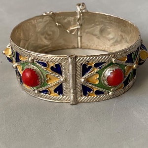May include: A silver bracelet with red, green, blue, and yellow enamel. The bracelet has a hinged clasp and is decorated with geometric patterns.