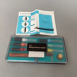 Könnte beinhalten: Ein türkisfarbenes Plastiketui mit schwarzem Deckel, das einen Satz Rapidograph-Zeichenstifte und Zubehör enthält. Das Etui trägt ein Etikett mit der Aufschrift "Pol Rapidograph".