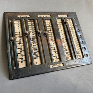 Può includere: Calcolatrice per maglieria in metallo vintage con cursori regolabili. La calcolatrice presenta scale per righe, aumento e volte, con numeri stampati. Il metallo ha un aspetto scuro e invecchiato con segni di usura.
