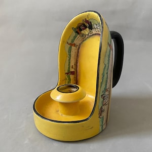 Könnte beinhalten: Ein gelber Kerzenhalter aus Keramik mit schwarzem Griff und Zierleiste. Der Kerzenhalter hat ein szenisches Design mit einer Pferdekutsche und Figuren. Der Kerzenhalter ist etwa 13 cm hoch.