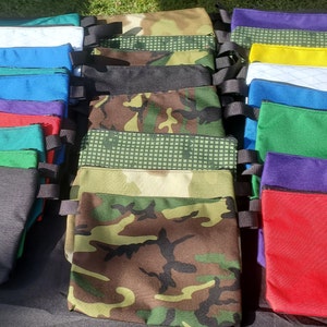 May include: A collection of colorful zippered pouches with various patterns, including camouflage, solid colors, and geometric designs. The pouches are made of fabric and have black straps.