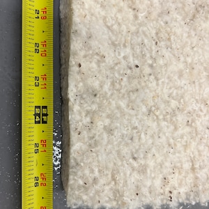 K&ouml;nnte beinhalten: Nahaufnahme eines wei&szlig;en, strukturierten Materials mit einem gelben Ma&szlig;band an der Seite. Das Band misst 68,58 cm.