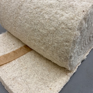 K&ouml;nnte beinhalten: Nahaufnahme einer Rolle wei&szlig;er Baumwollwatte. Die Watte ist fest gepackt und hat eine leicht raue Textur. Die Rolle ist teilweise abgerollt und zeigt das weiche, flauschige Material im Inneren.