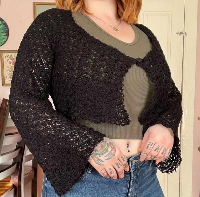 May include: Black crochet cardigan with a loose fit and bell sleeves. The cardigan is open in the front and has a single button closure.