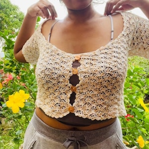 May include: A white crochet top with a brown button closure. The top has a scalloped hem and short sleeves.