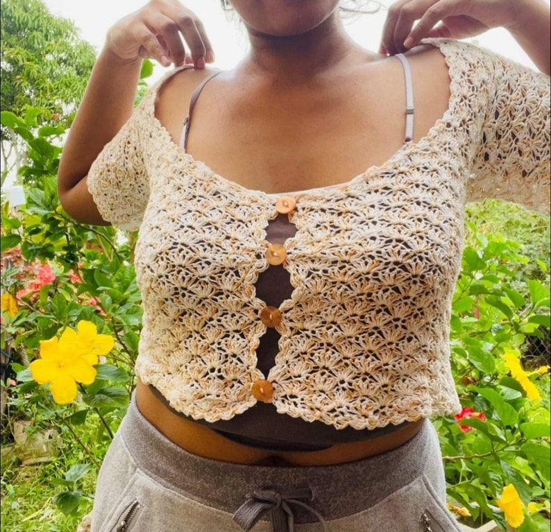 May include: A white crochet top with a brown button closure. The top has a scalloped hem and short sleeves.