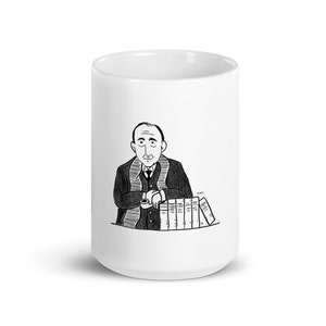 May include: A white coffee mug with a black and white illustration of a man with a pipe in his hand, sitting at a table with a stack of books in front of him.