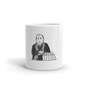 May include: A white ceramic mug with a black and white illustration of a man with a mustache wearing a suit and scarf, holding a cup in his hand. The man is sitting at a table with a stack of books in front of him.