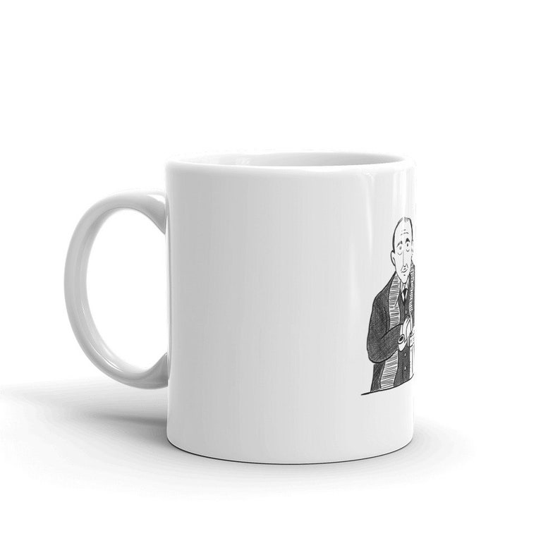 May include: A white ceramic mug with a black and white illustration of a person wearing a scarf and suit jacket. The person is looking to the right and has their hands clasped in front of them.