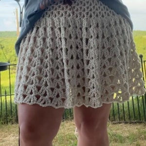 May include: Cream-colored crochet skirt with a scalloped hem. The skirt is made of a light, open-weave material, creating a textured appearance. The skirt is a mini-skirt style.